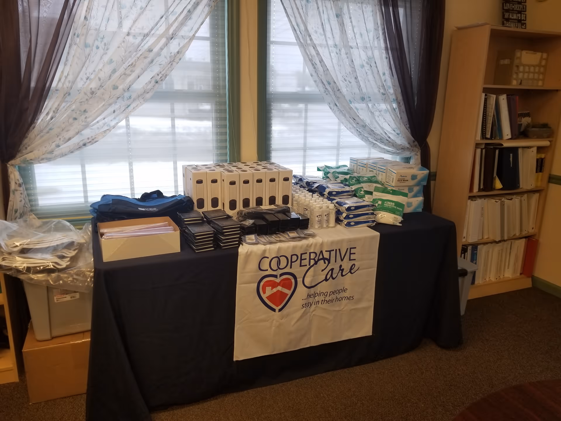 A table with a Cooperative Care banner holds assorted medical supplies in a room.