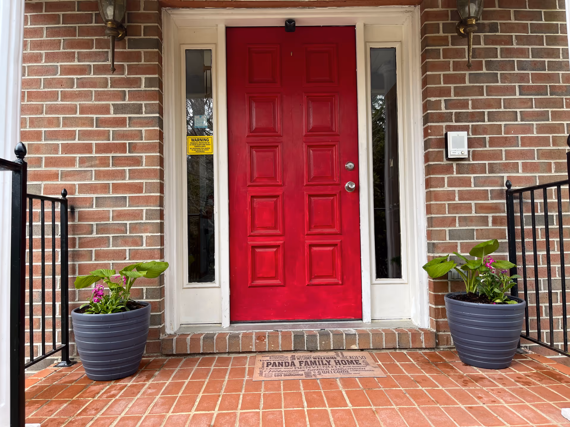 Brick front porch with a bright red door and two planters by the steps.