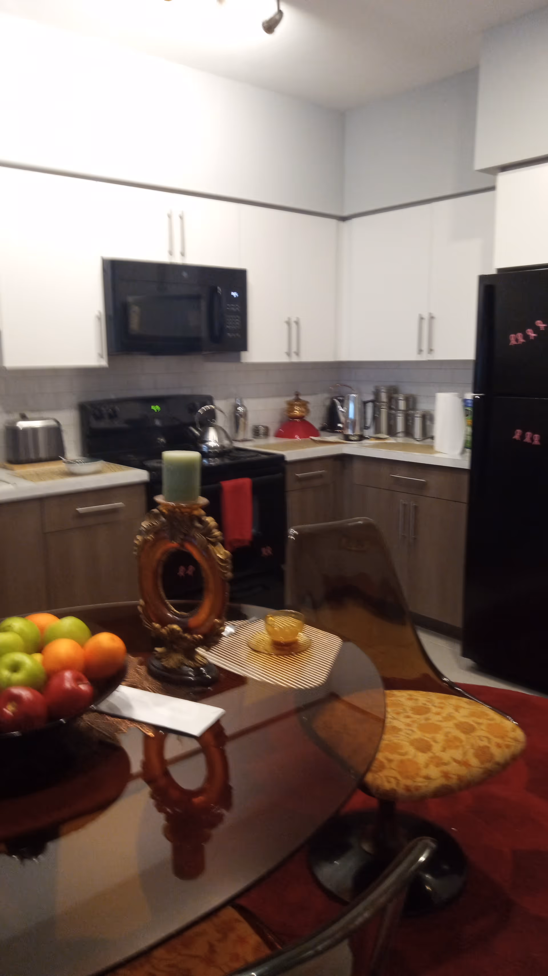 Modern kitchen with white cabinets, black appliances, glass dining table, fruit bowl, and candle centerpiece.