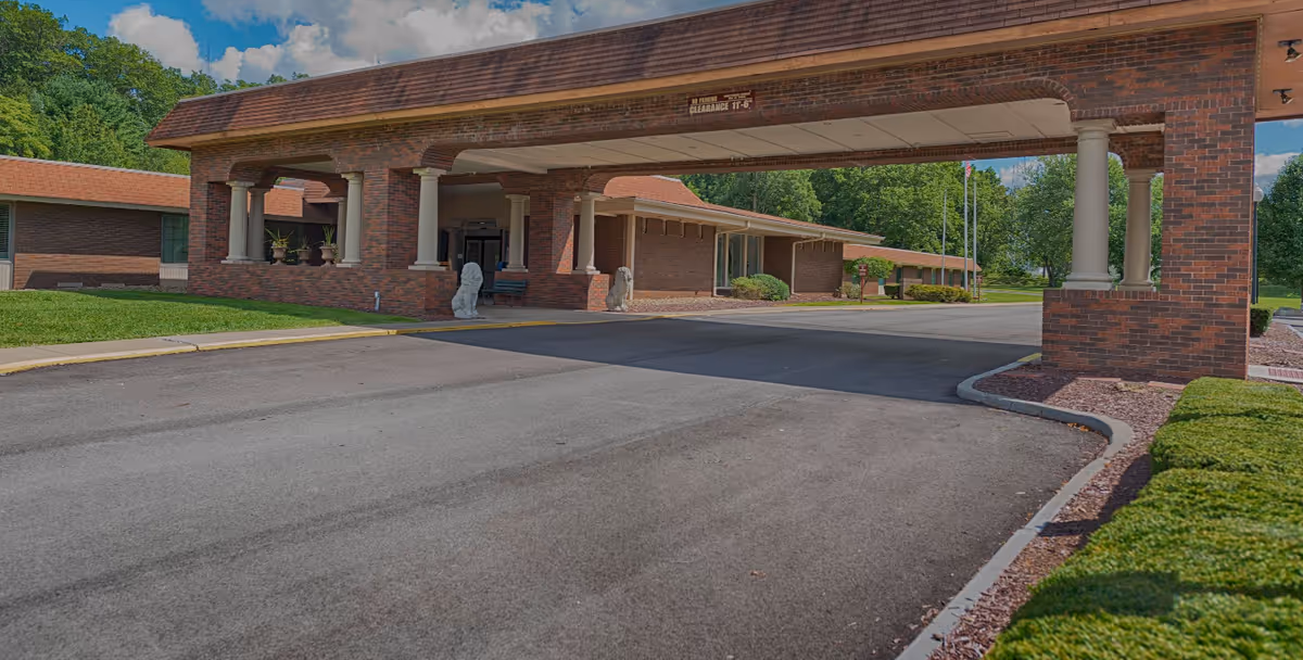 Brick facility entrance with a covered drive-through and landscaped surroundings.