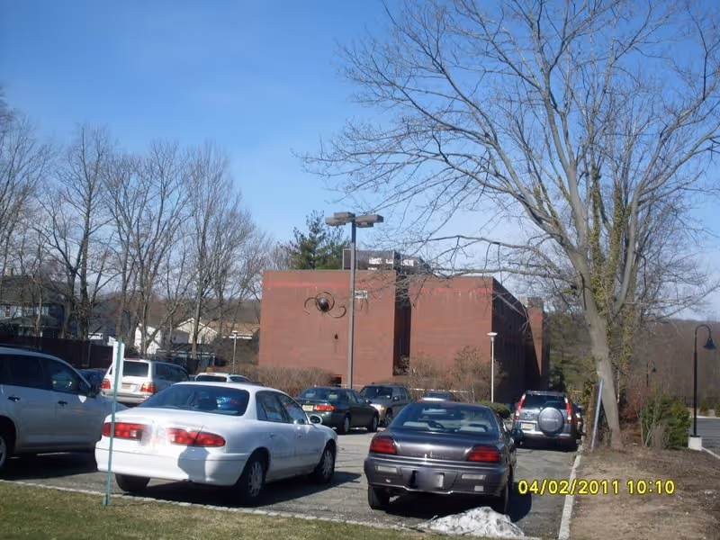 Parking lot in front of a brick building with leafless trees under a blue sky.