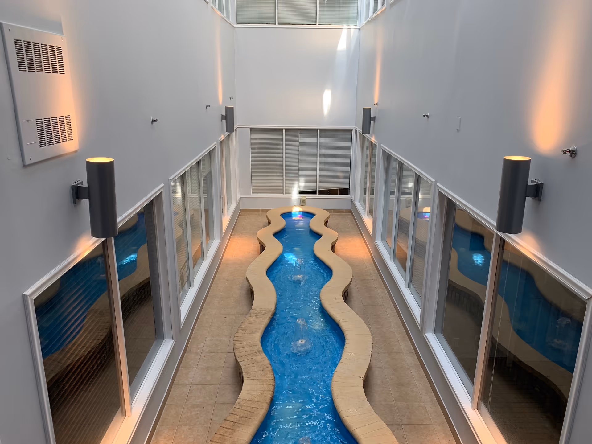 Indoor winding pool in a bright, modern atrium with glass walls and warm lighting.