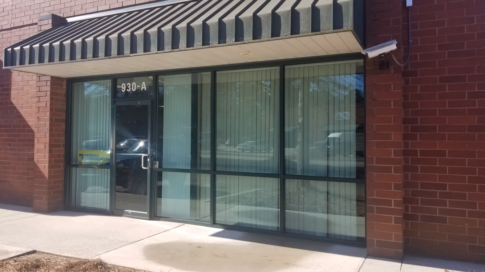 Exterior brick entrance with large glass doors under a striped awning.