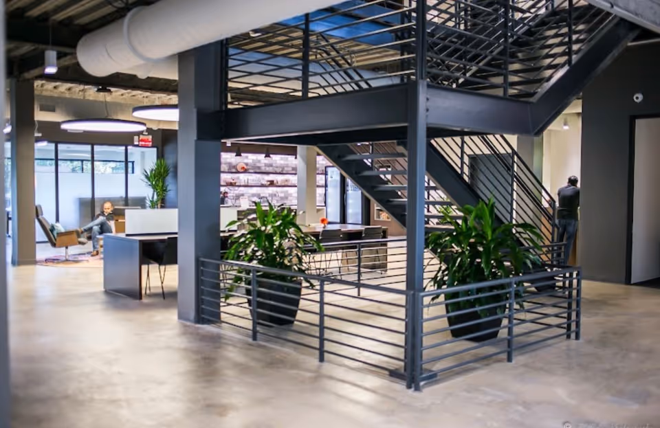 Modern open lobby with metal staircase, large planters, and seating areas in a contemporary space.