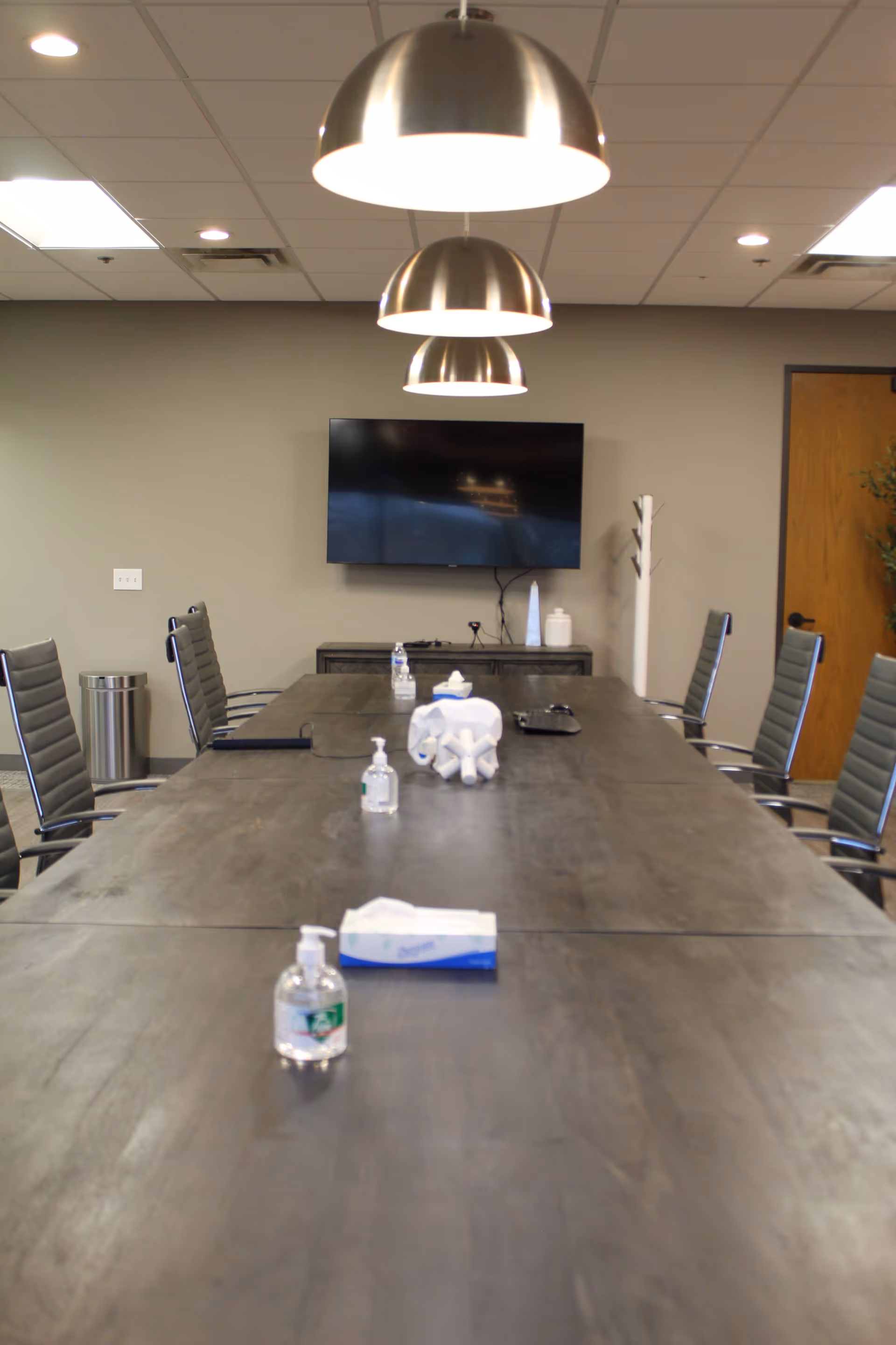 A long conference table with chairs, a wall TV, pendant lights in a modern meeting room.
