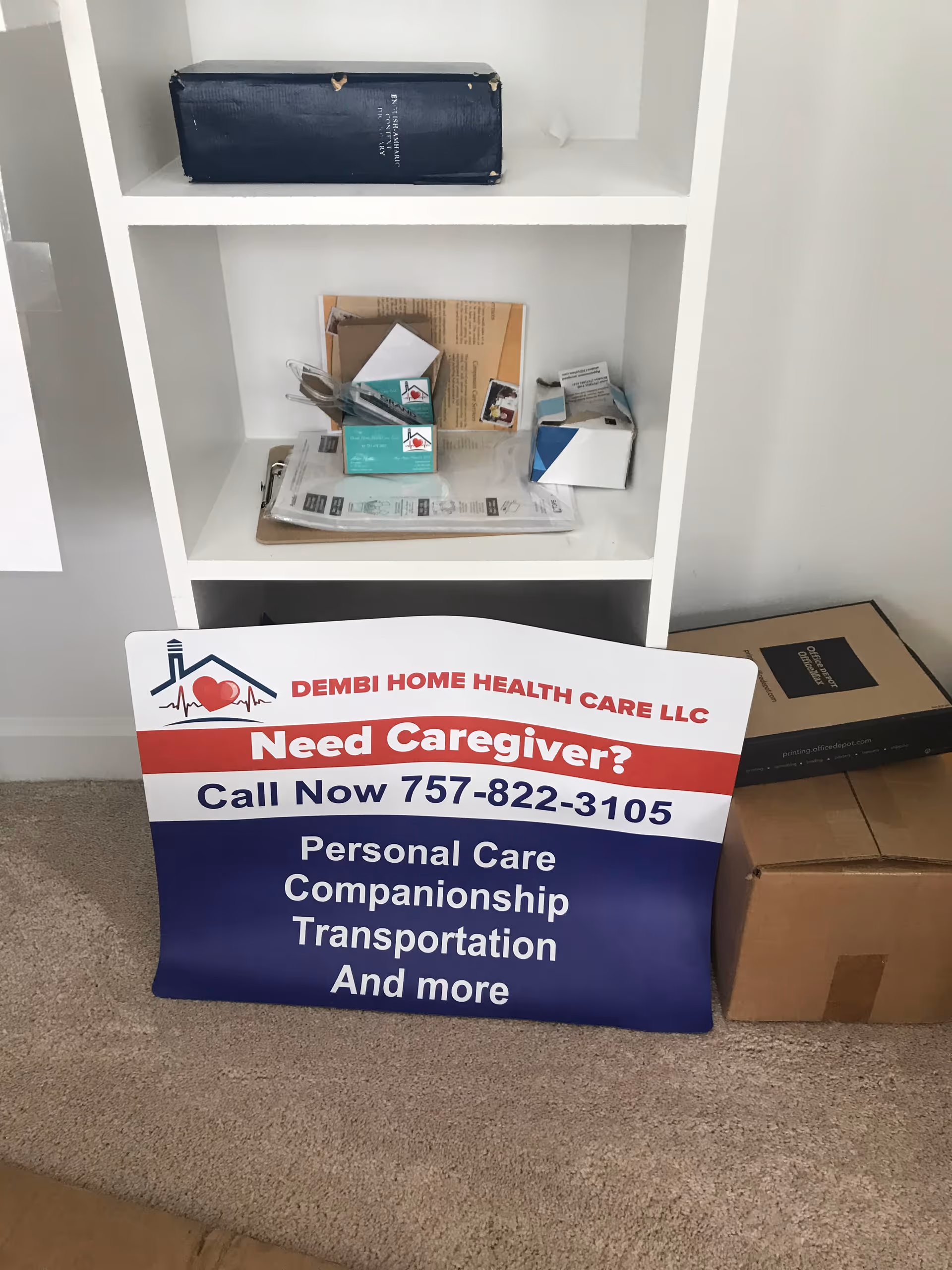Advertisement sign for Dembi Home Health Care LLC on carpet beside a white shelving unit.