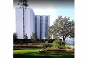 Tall white high-rise building with landscaped lawn and trees.