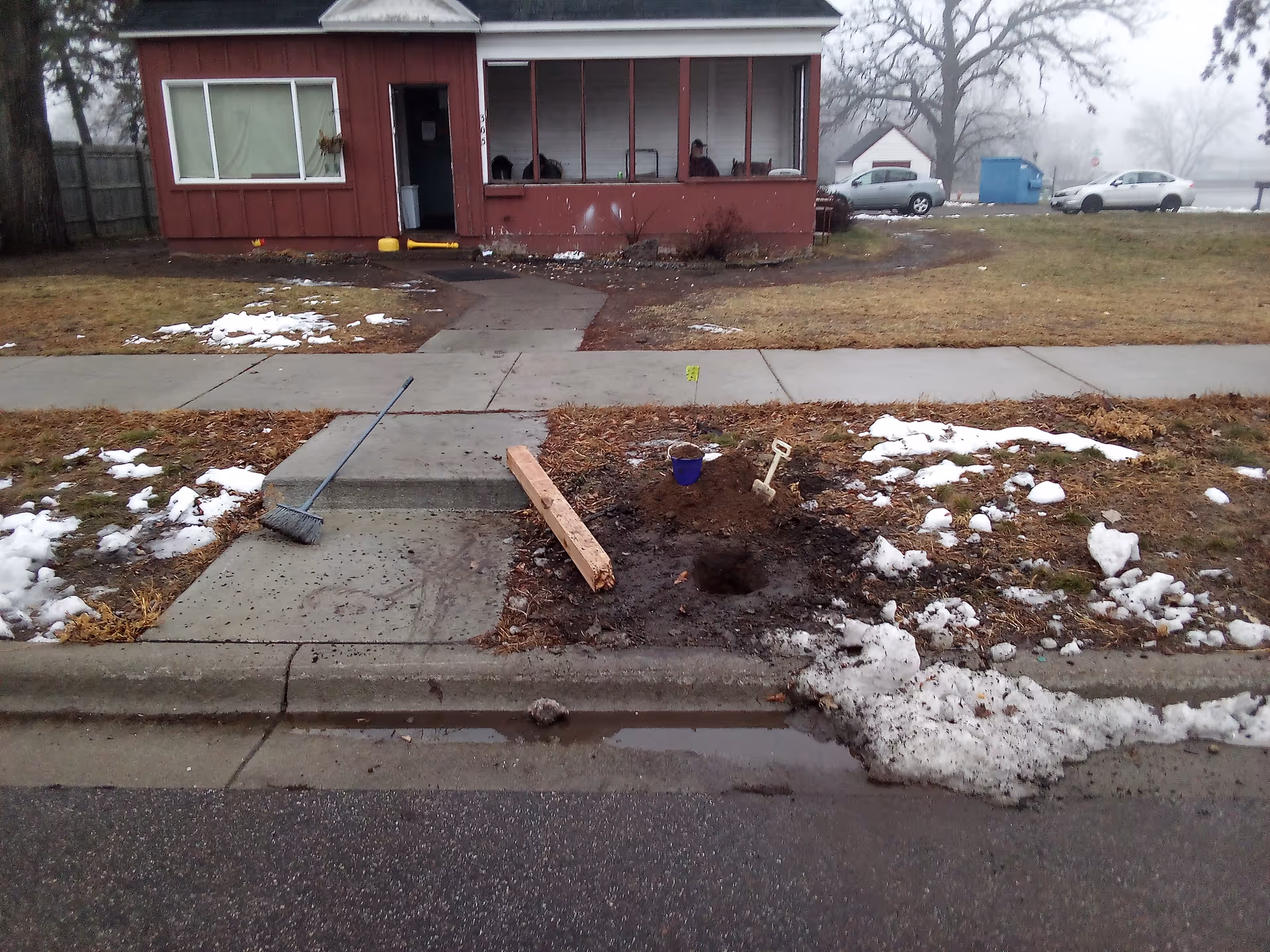 Red single-story building with a large front window, sidewalk, and a dug hole in the yard.