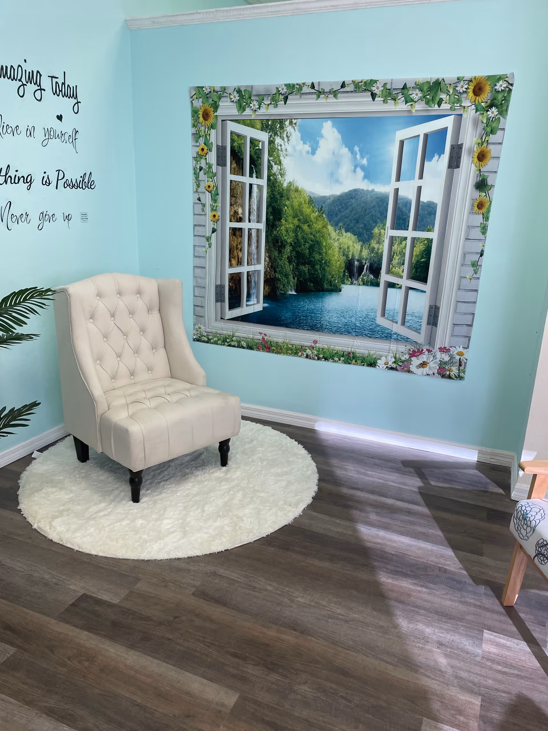 Light turquoise lounge area with tufted cream chair, white rug, and scenic window mural.