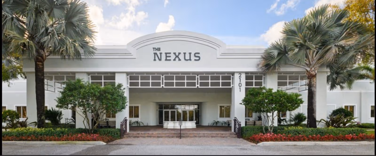 Front view of a modern building entrance labeled The Nexus with palm trees and landscaping.