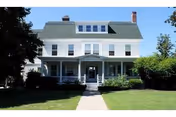 White two-story house with a green roof and front porch on a grassy lawn.