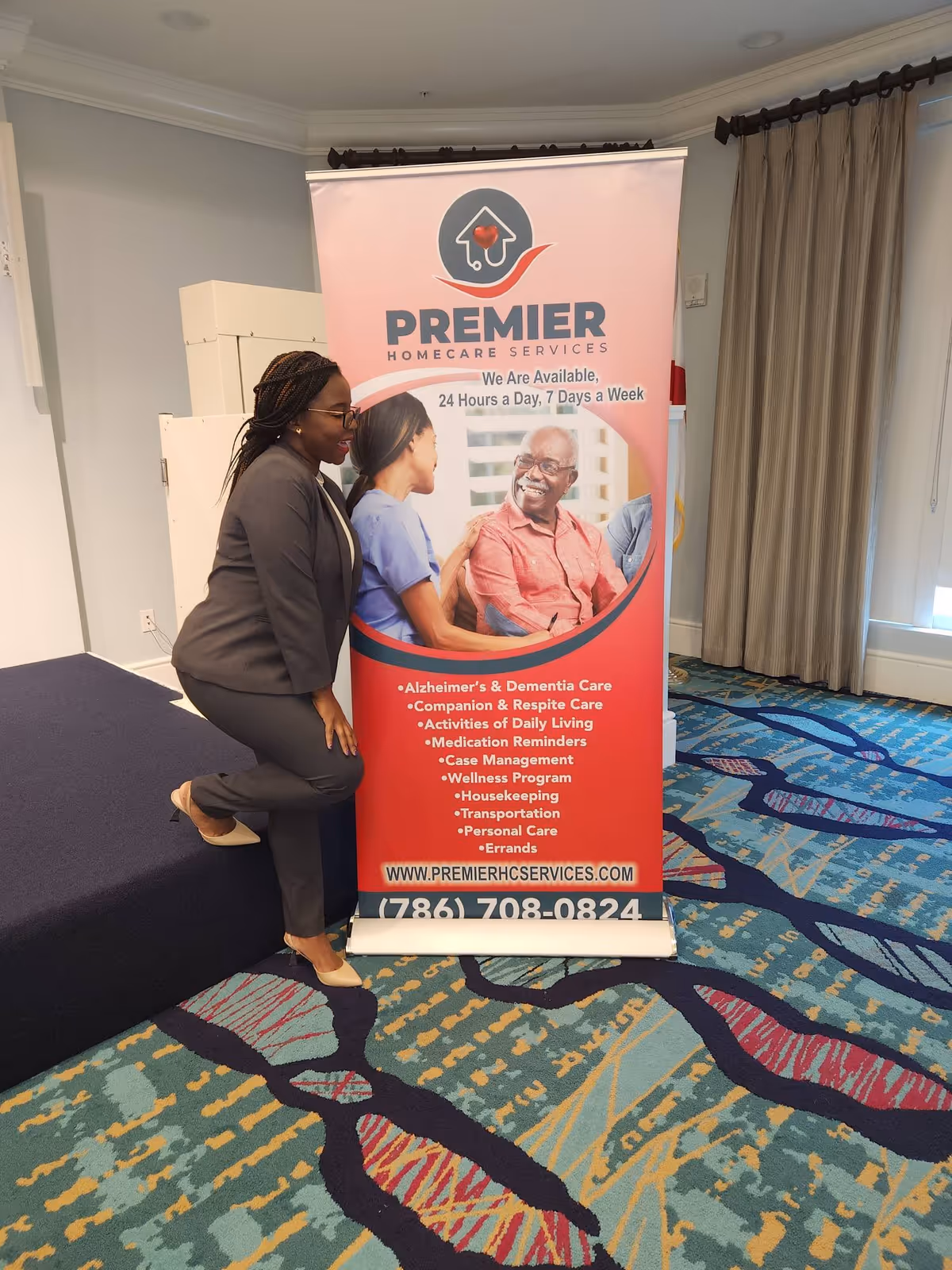 A woman in business attire leans on a stage beside a Premier Homecare Services banner indoors.