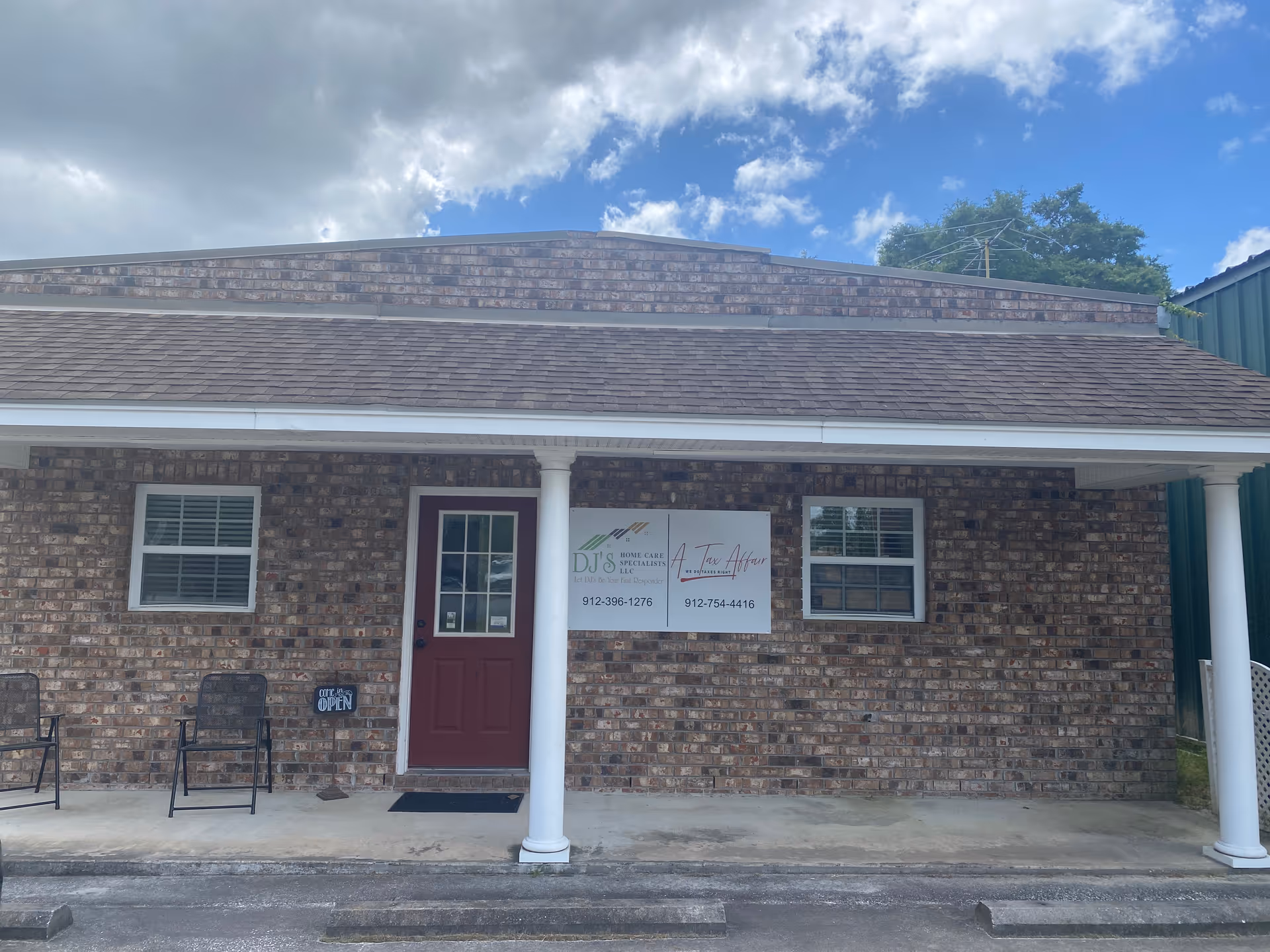 Brick building storefront with DJ's Home Care Specialists LLC sign, red door, and two chairs outside.