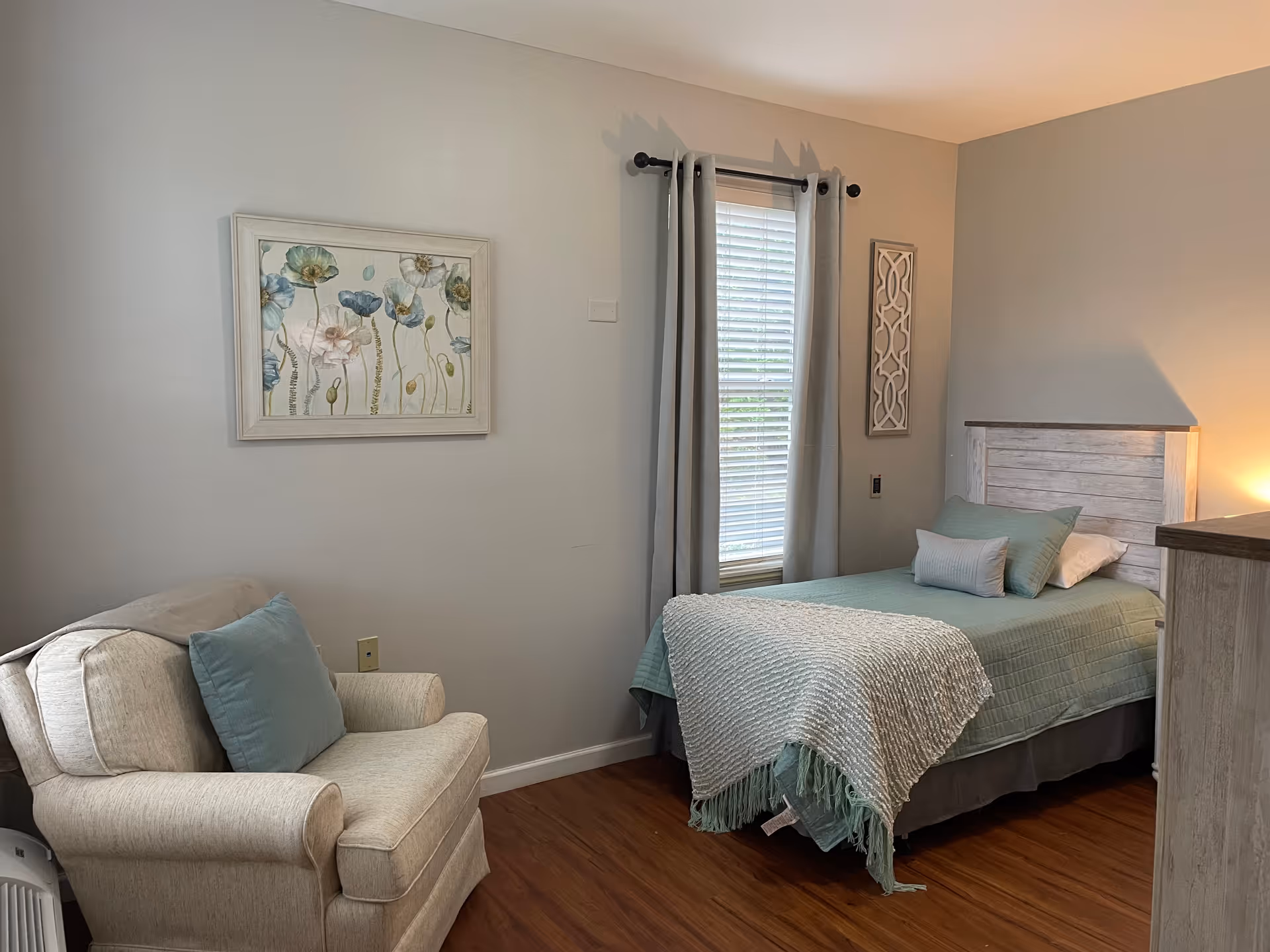 A cozy bedroom with a single bed, chair, dresser, and pale blue decor.