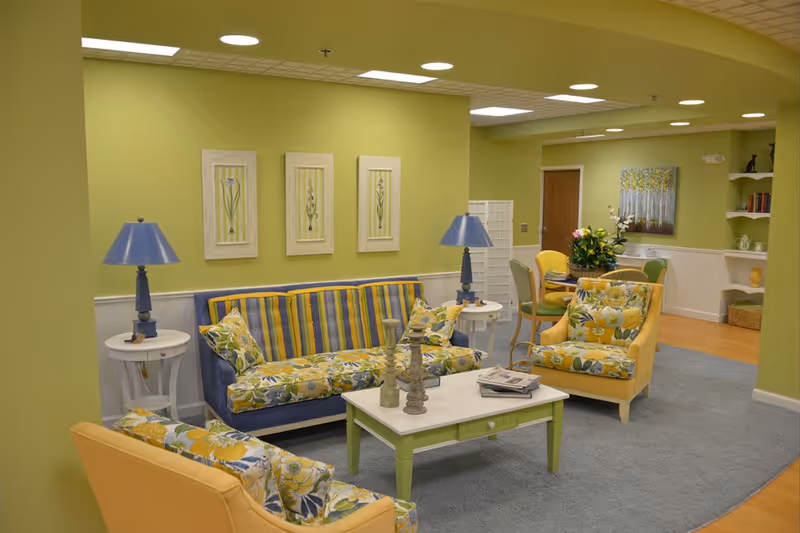 Bright lime-green walls in a senior living lounge with striped sofa, yellow chairs, and coffee table.