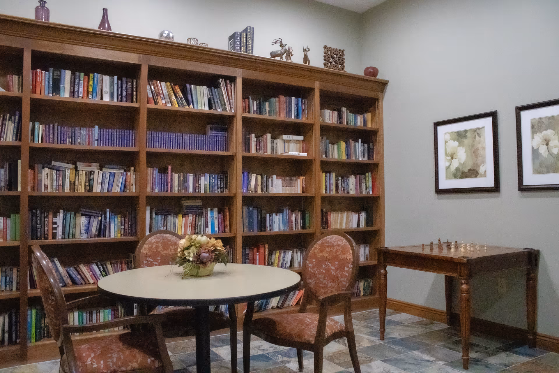 Cozy reading room with tall wooden bookshelves, round table, chairs, and a chess table.