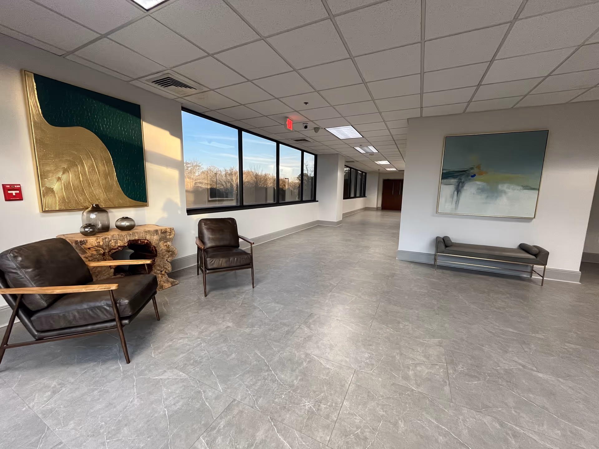 Modern, spacious lobby with leather chairs, abstract art, and a windowed hallway.