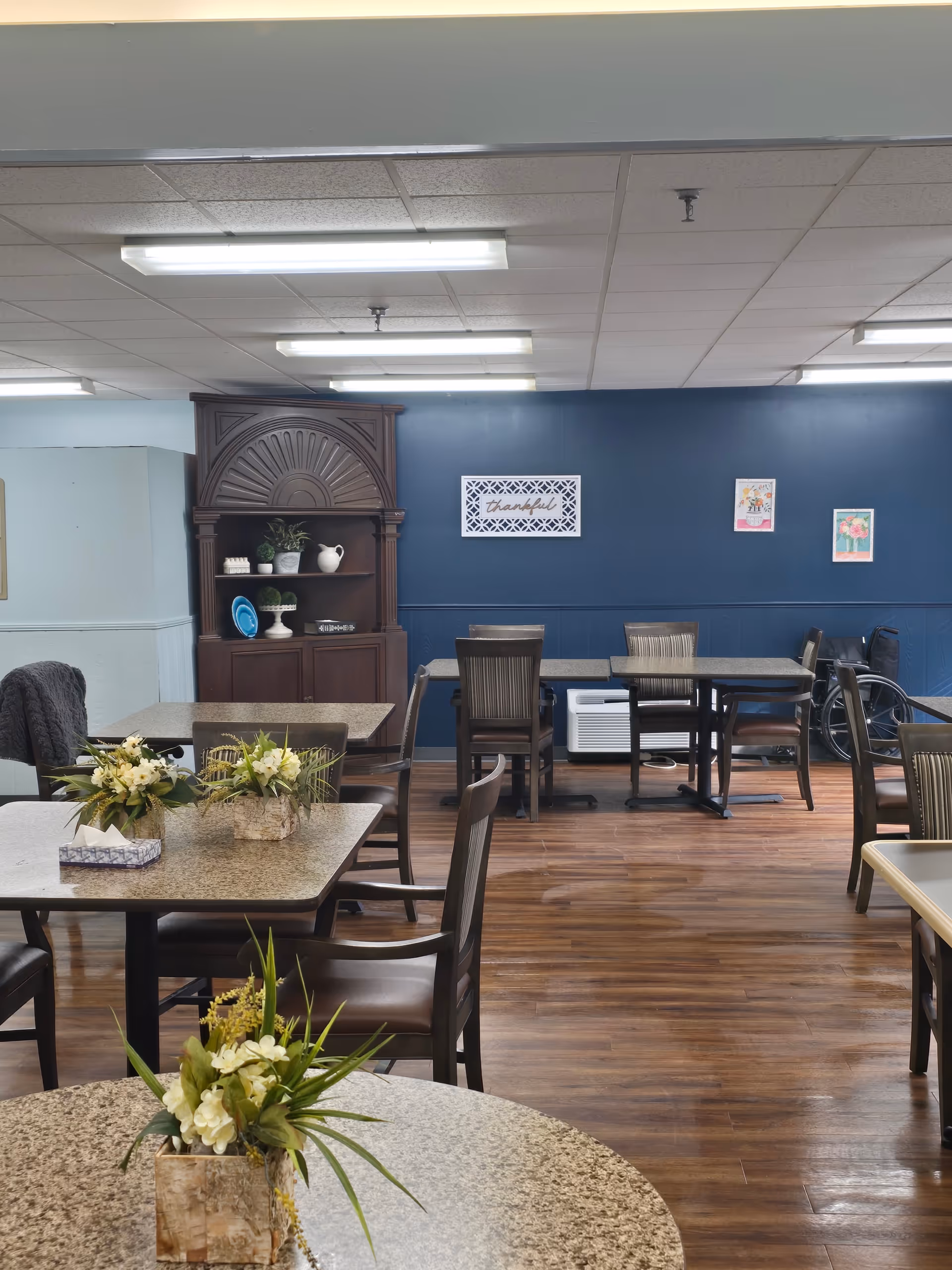 A senior living dining room with tables, chairs, and a blue accent wall.