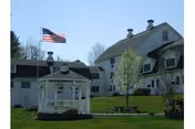 White senior living buildings with a gazebo, flag, and manicured lawn in front.