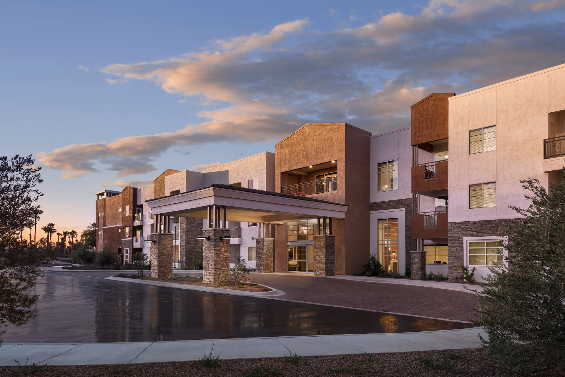 Senior living facility exterior with covered entrance and curved driveway at sunset