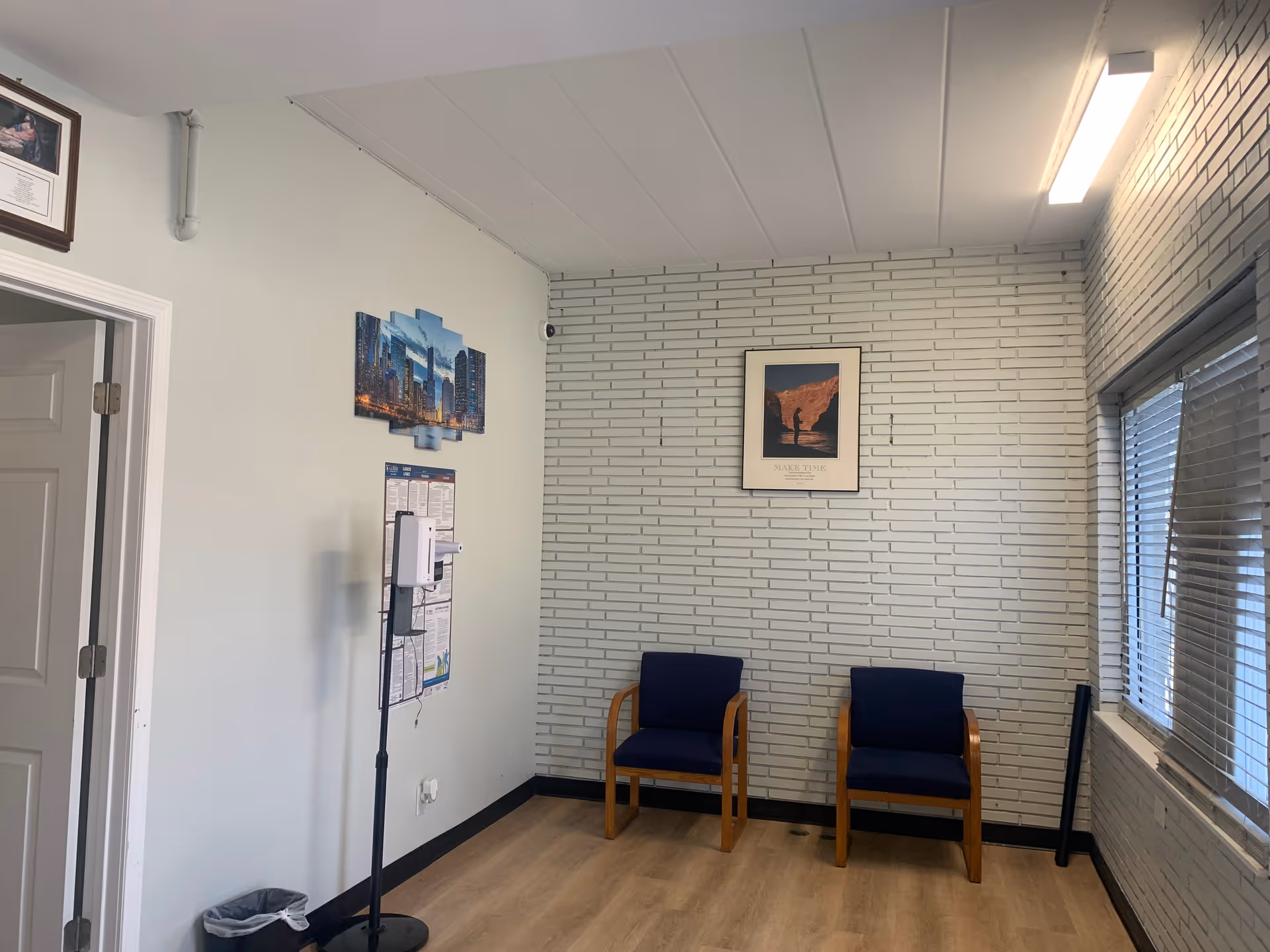Waiting area with two blue chairs along a brick-walled interior, windows, and wall decor.