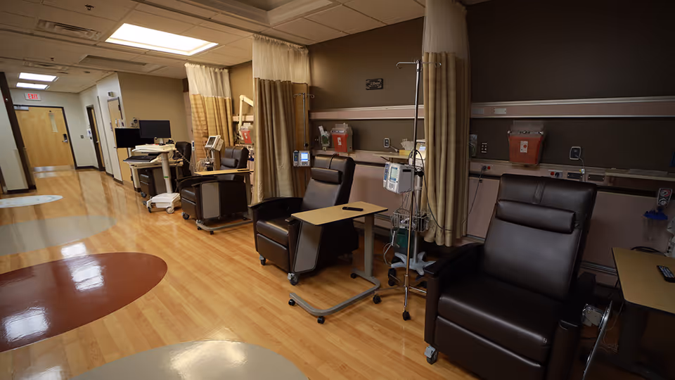 Interior hospital infusion area with brown recliner chairs, IV poles, curtains, and medical equipment.