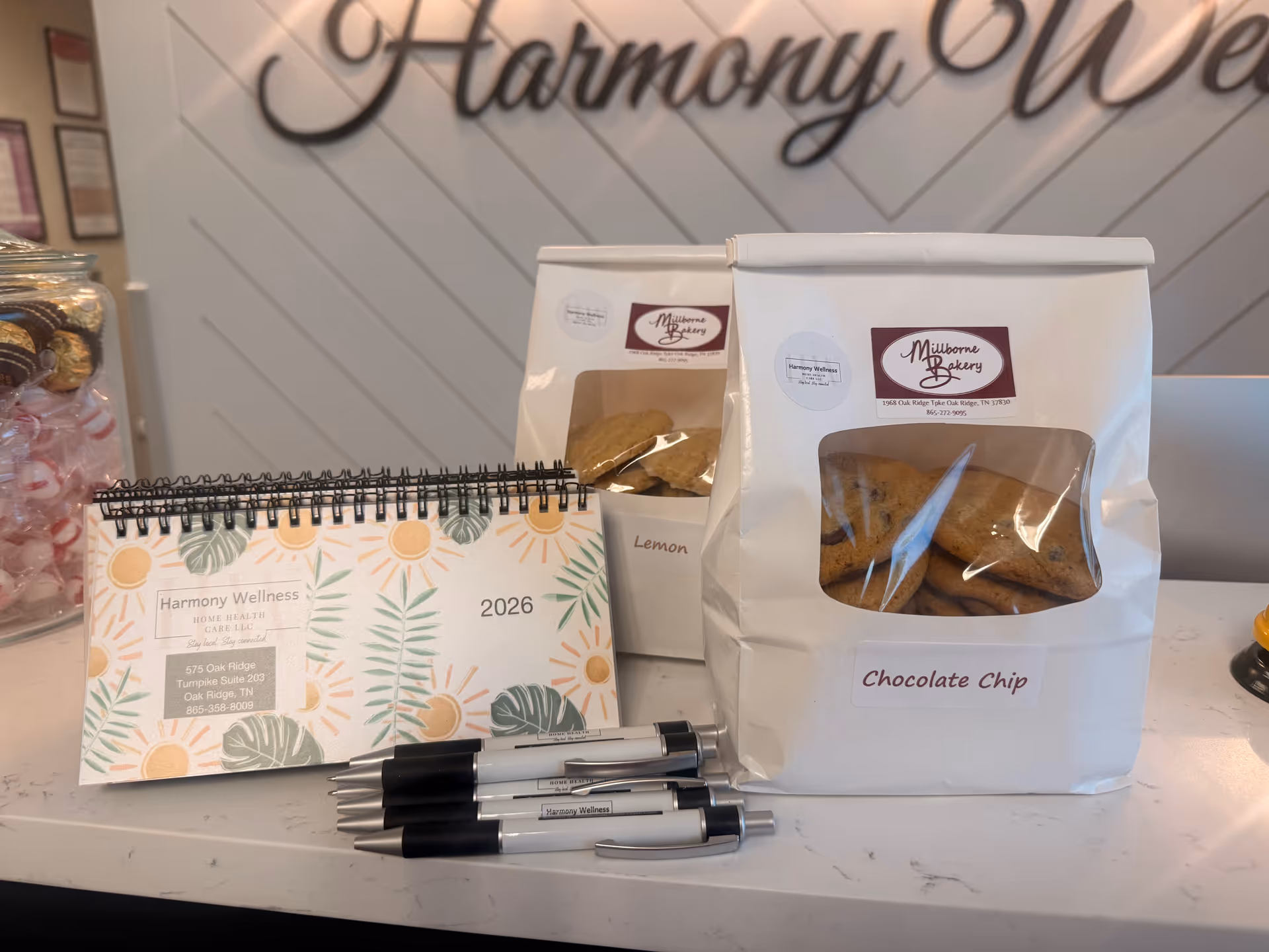 Reception counter with cookie bags, a 2026 Harmony Wellness calendar, and pens.