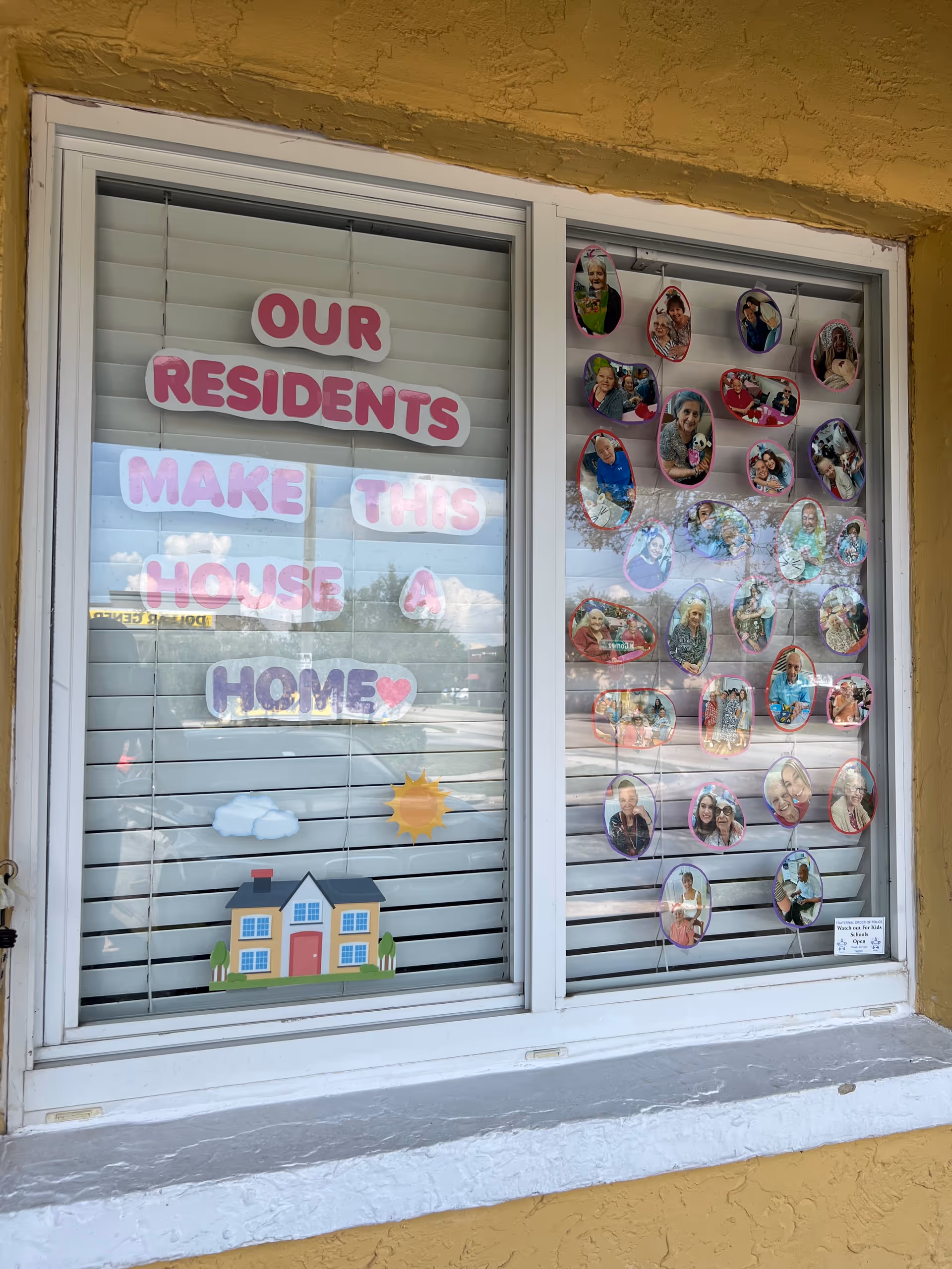 Window display on building with residents' photos and message 'Our Residents Make This House A Home'.