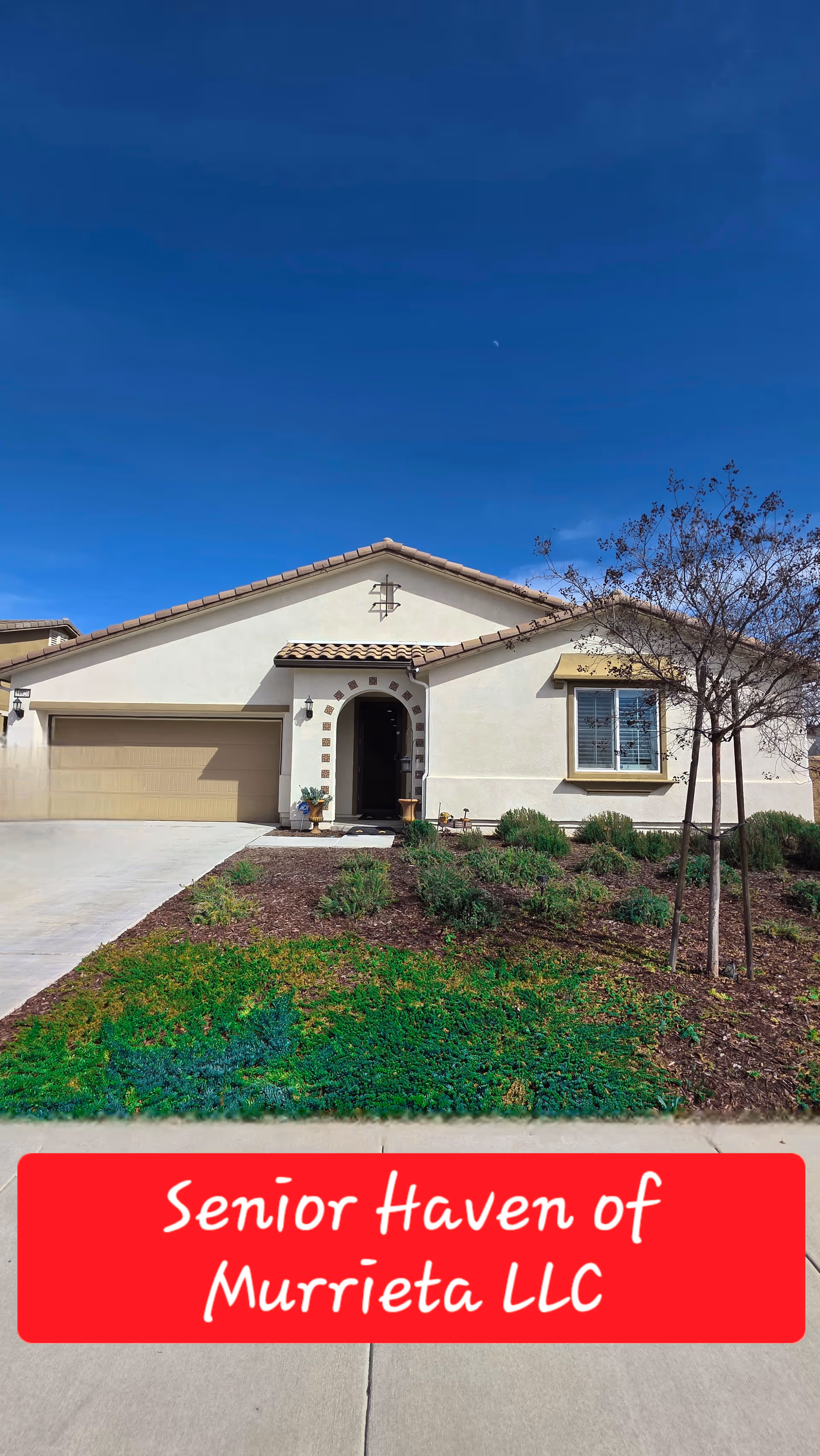 Front view of a beige single-story house with a driveway, yard, and red banner.