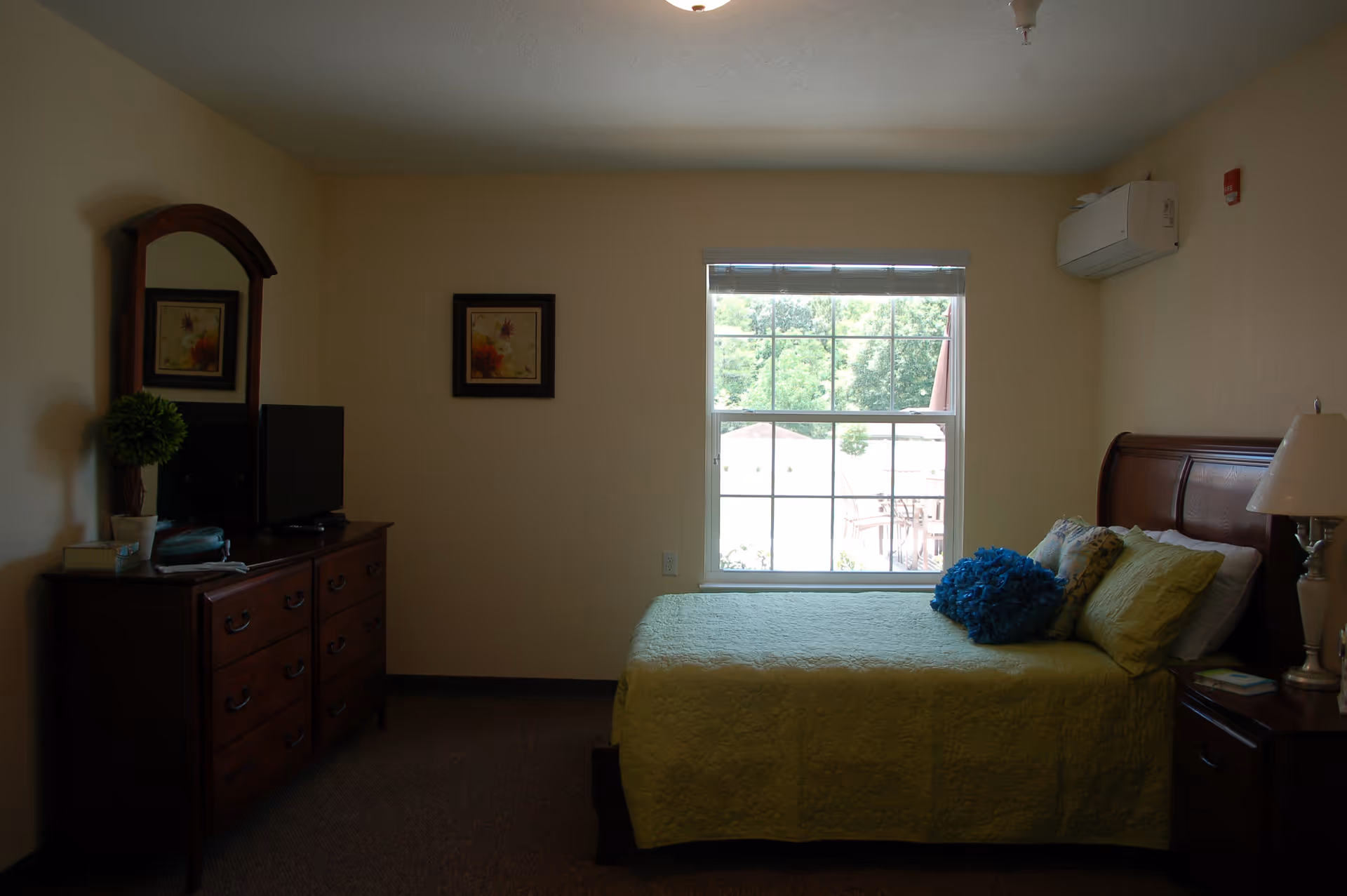 Bedroom in a senior living facility featuring a bed, dresser, and window.
