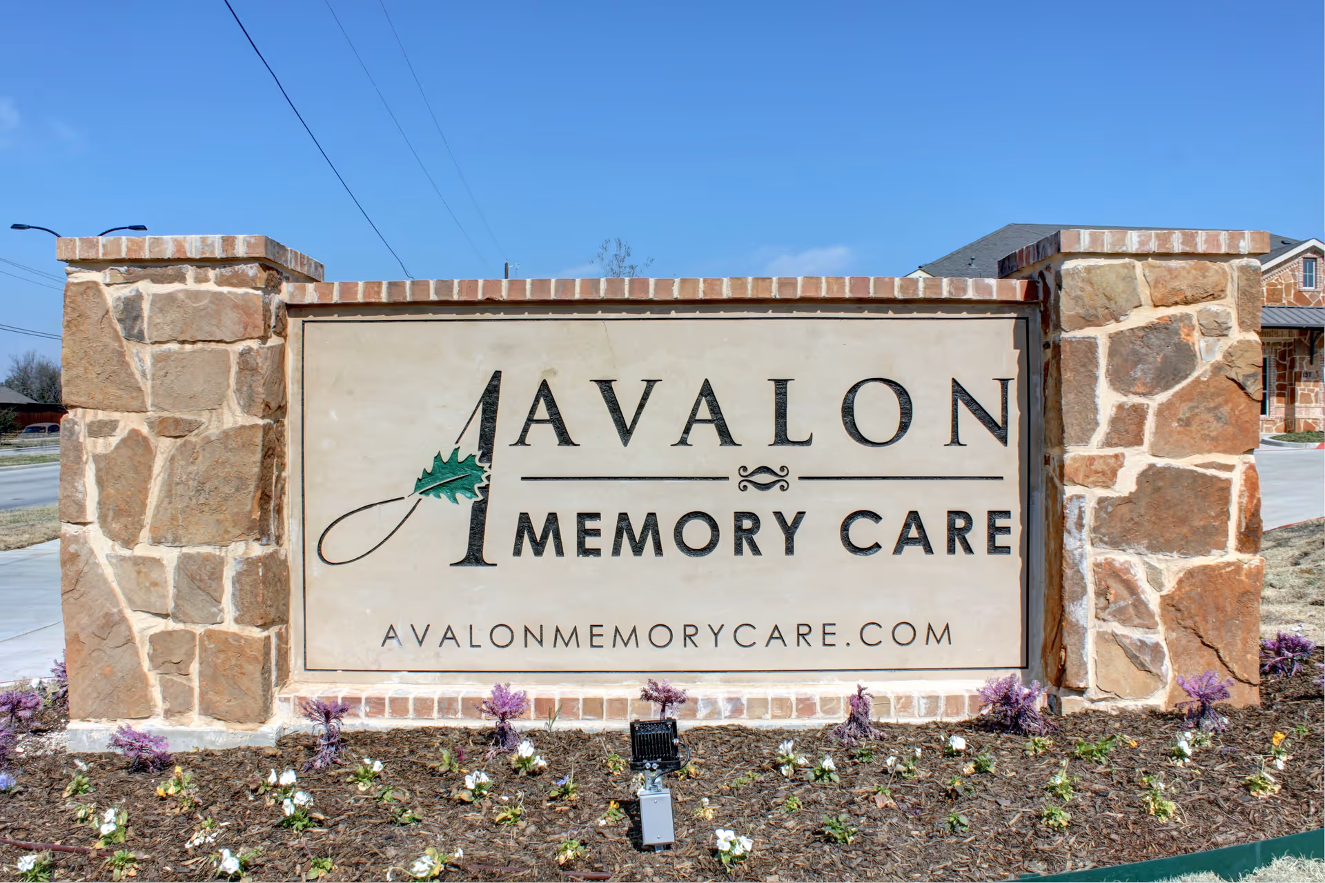 Stone Avalon Memory Care sign at the facility front with blooming flowers.