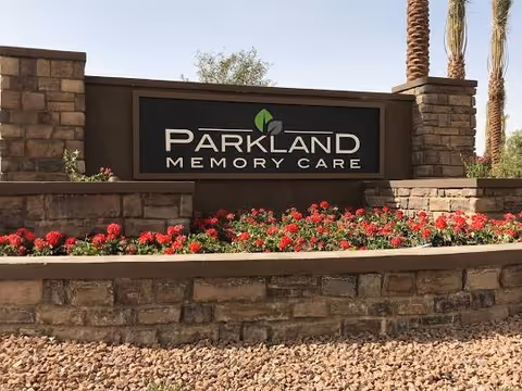 Parkland Memory Care sign mounted on a stone wall with flowers and palm trees.