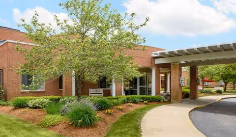 Brick senior living facility with a covered entrance, walkway, and landscaped front yard.