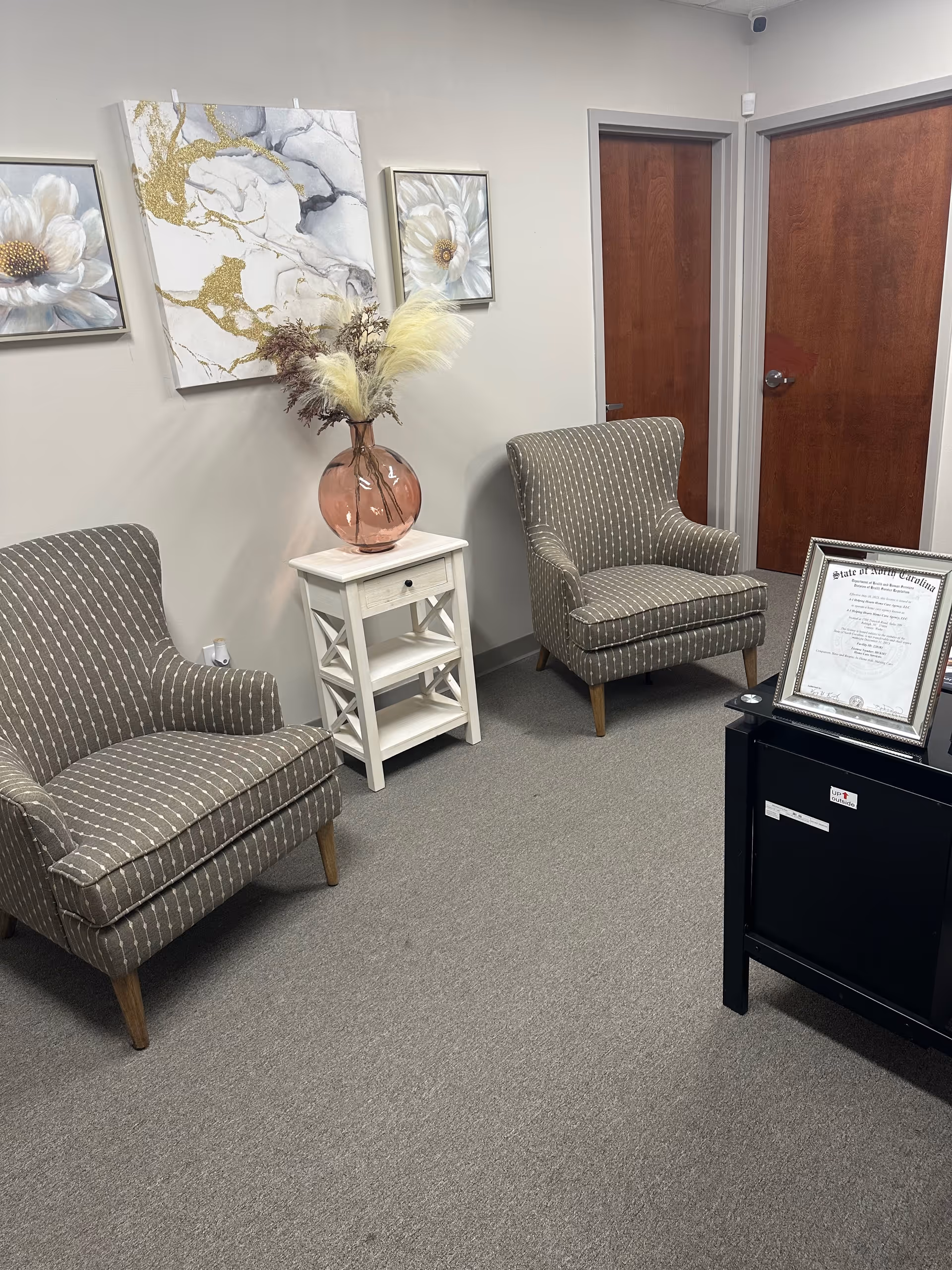 A small waiting area with two patterned chairs, a white side table, and floral wall art.