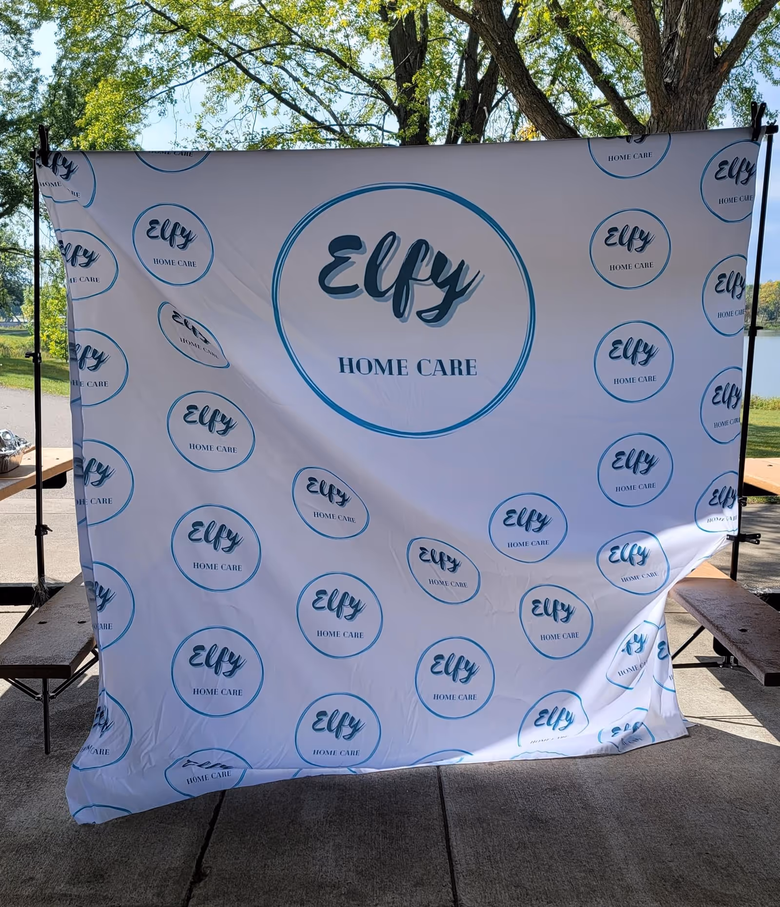 Outdoor event backdrop featuring Elfy Home Care logos with two benches on each side.