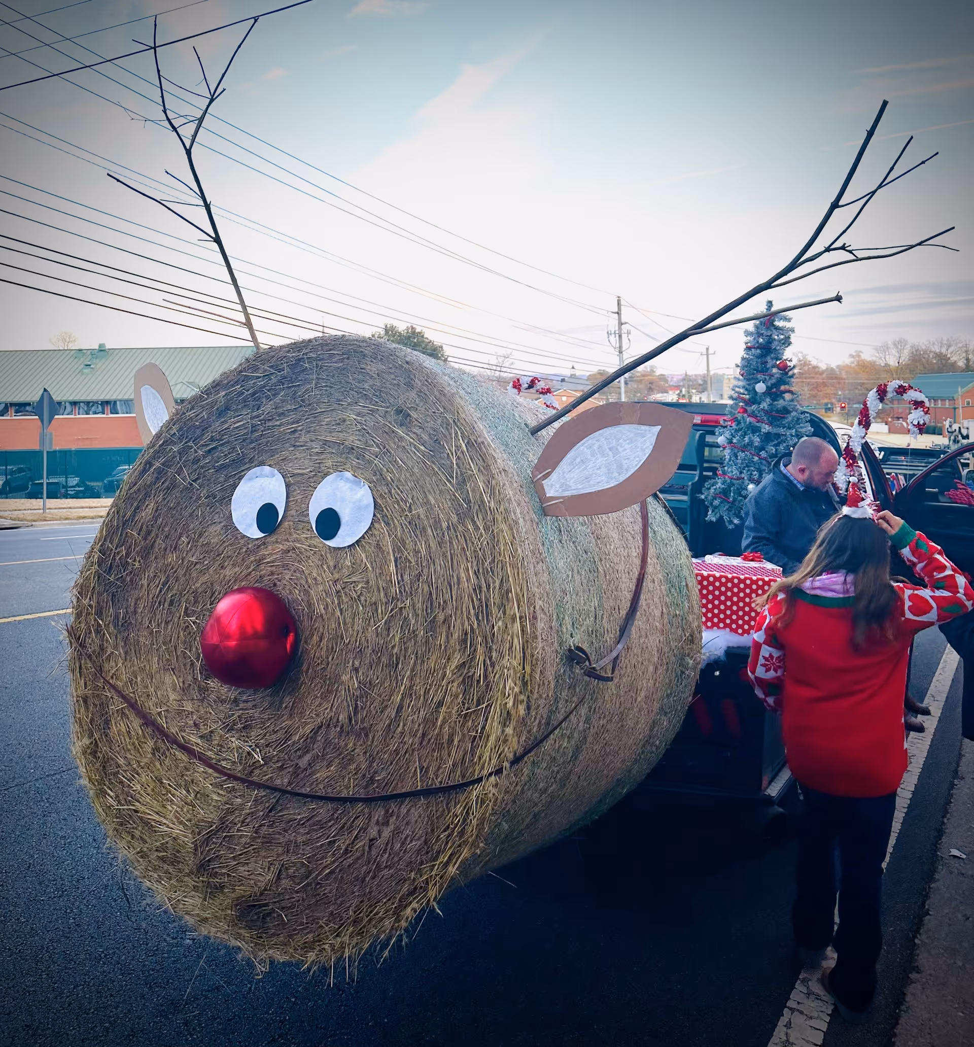 A giant hay bale reindeer float on a street with people and festive decorations.