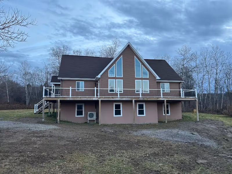 Two-story brown house-style senior living facility with a wraparound deck and bare trees.