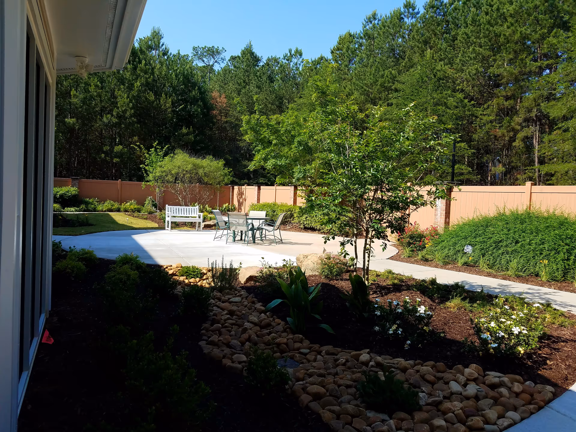 Outdoor patio with table and chairs, a white bench, and landscaped garden near a privacy fence.