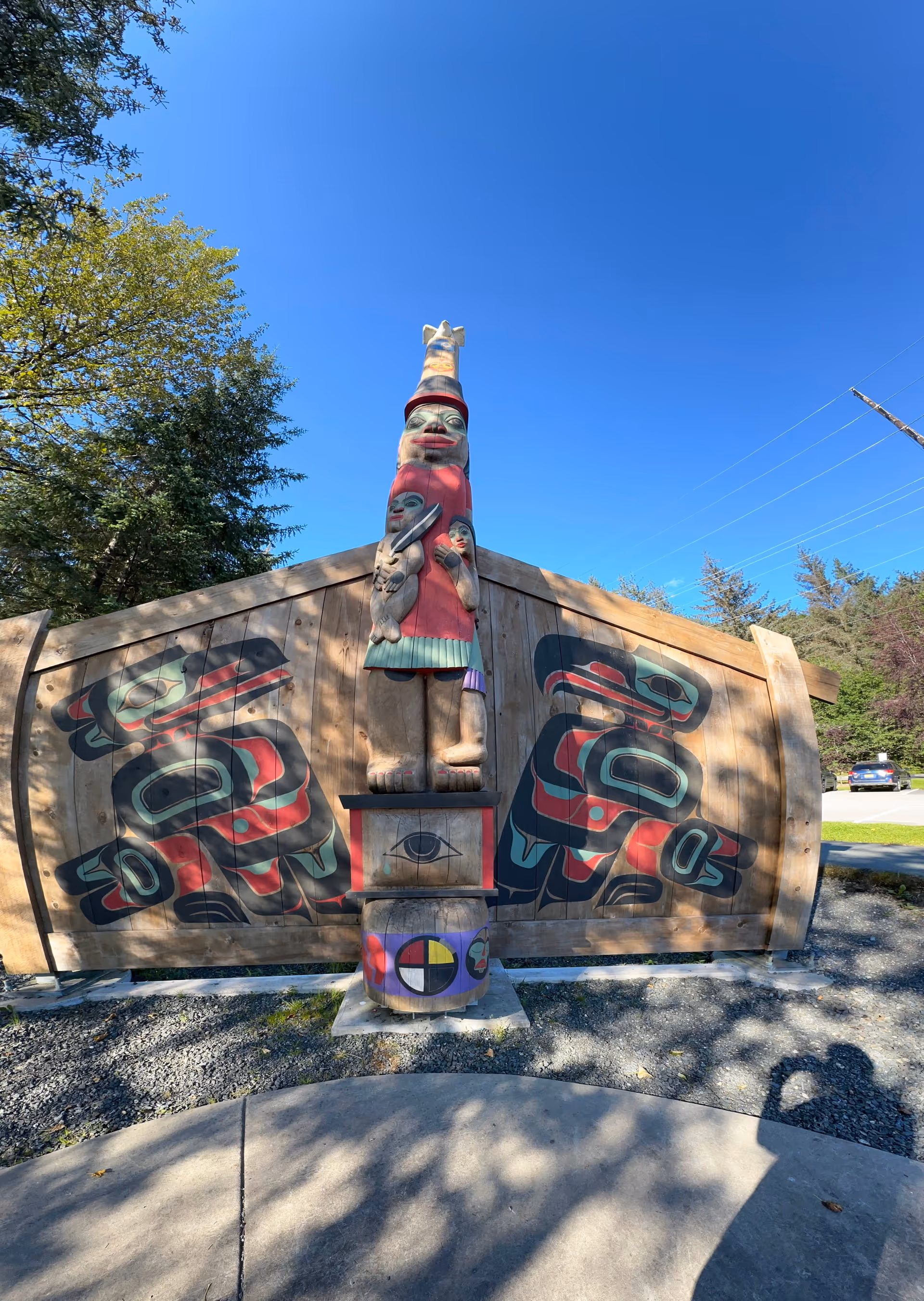 Outdoor view of a carved totem statue with painted panels against a blue sky.