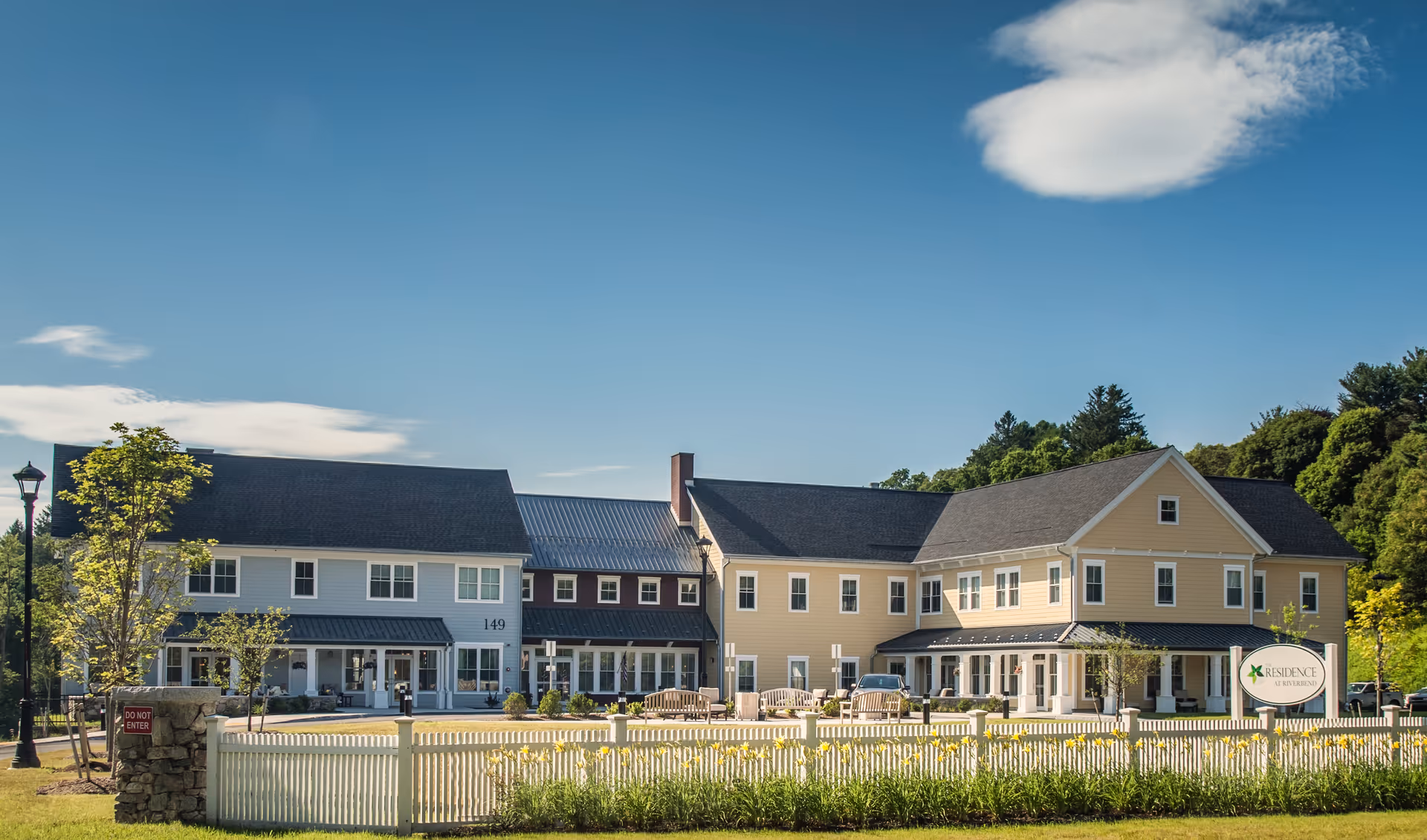 Exterior view of a multi-wing senior living facility with a white picket fence and blue sky