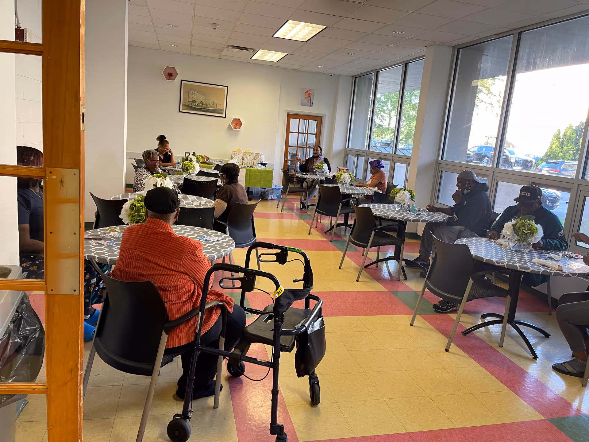 Residents sit at round tables in a bright dining room with floral centerpieces.
