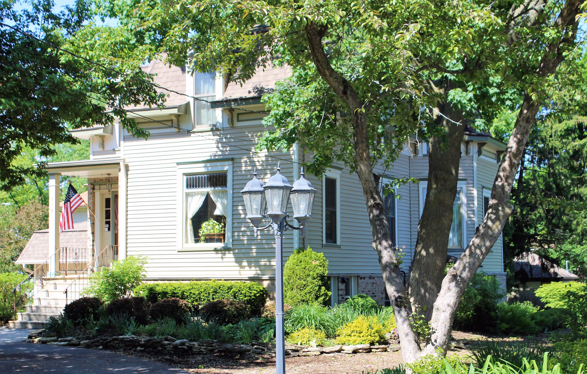 Exterior view of a light-colored house with landscaping, flag, and a decorative lamp post.