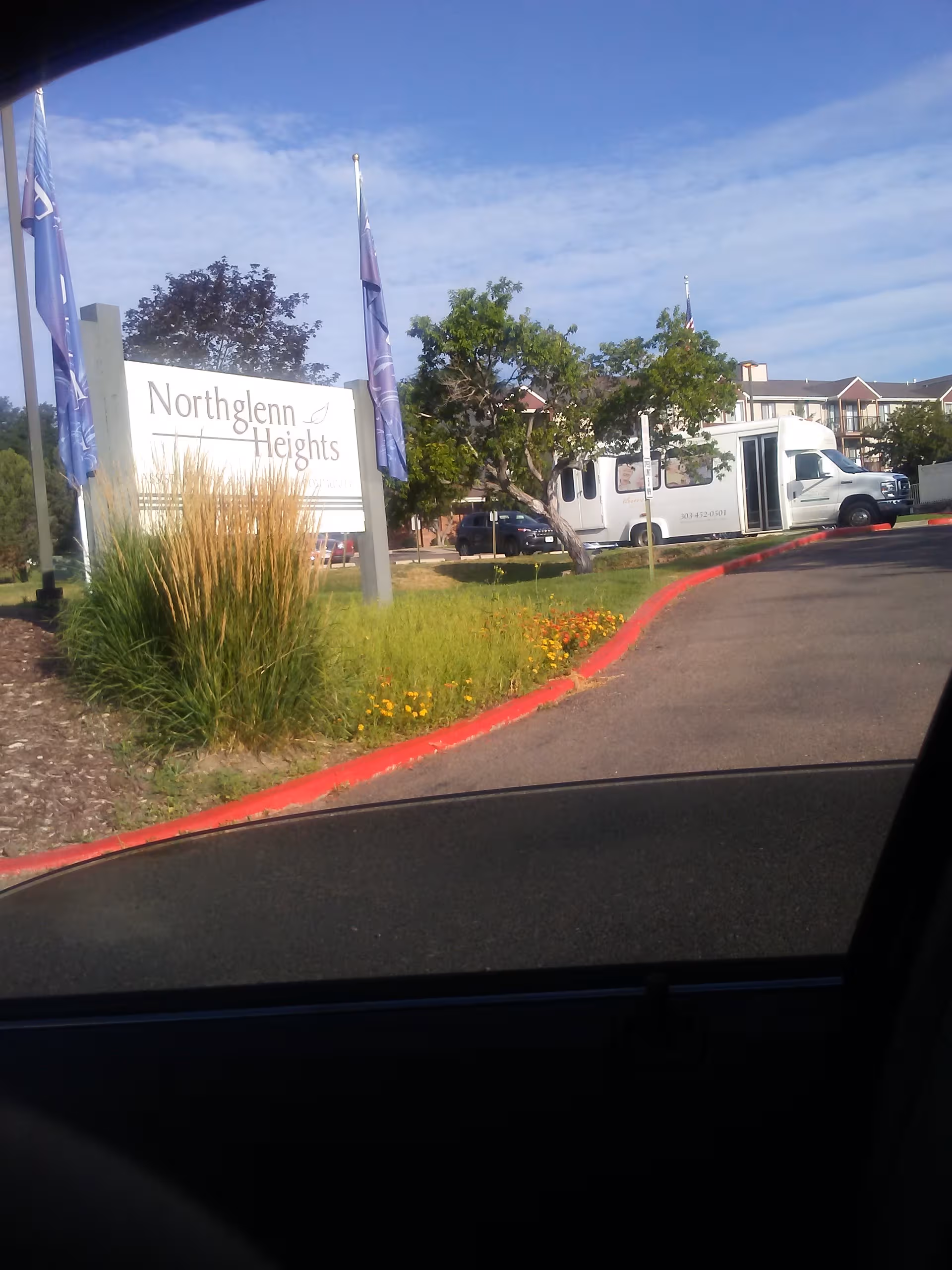 Northglenn Heights sign with flags and a shuttle bus at the facility entrance.