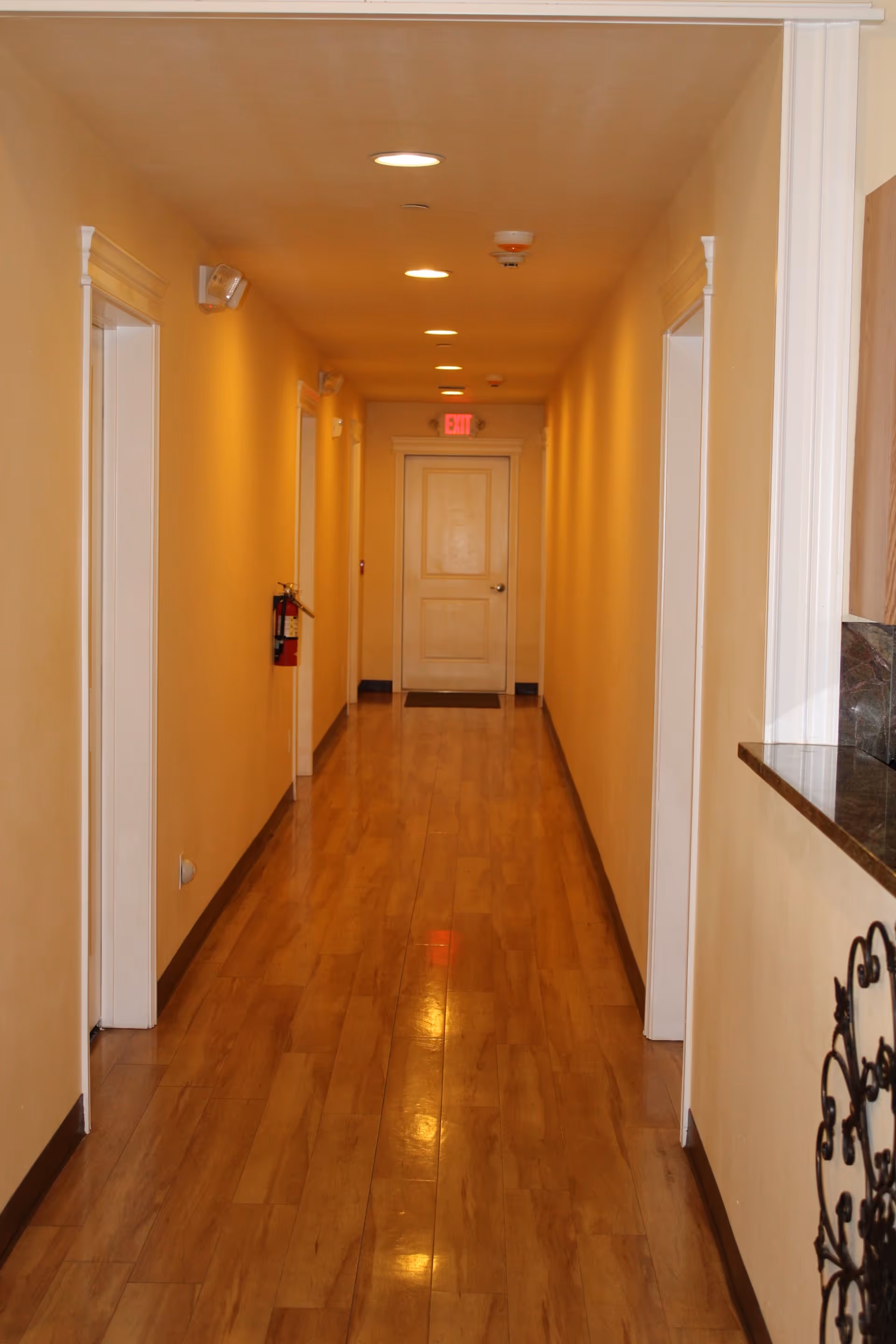 Long, well-lit hallway with doors along beige walls and wooden flooring.