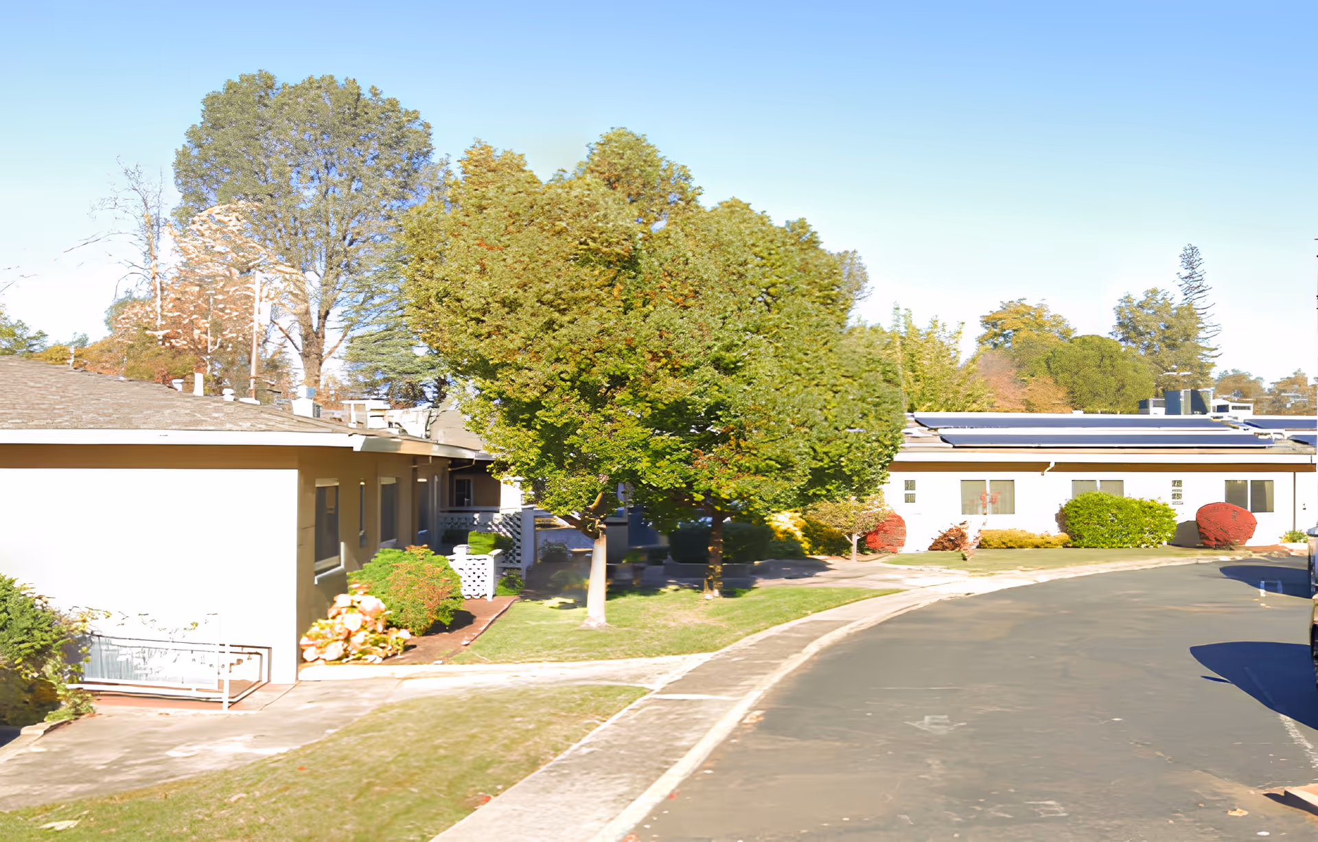 Single-story senior care facility exterior with landscaped lawns, trees, and a curved driveway.