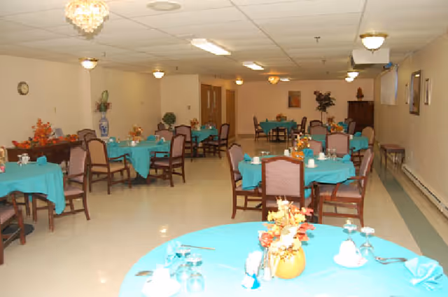 Dining room with multiple round tables covered in turquoise tablecloths and set with dinnerware, surrounded by chairs.