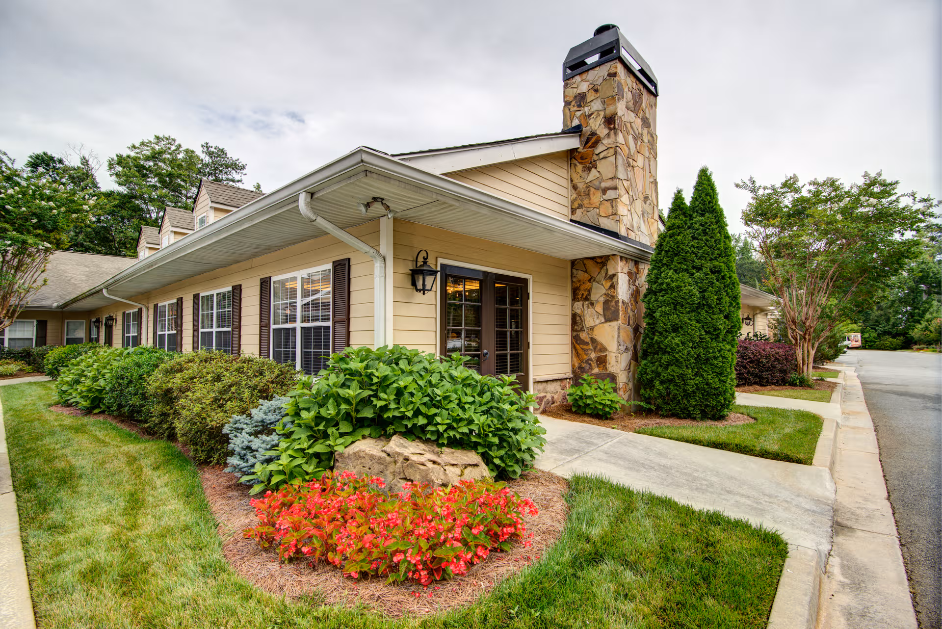 Exterior view of a senior living facility with stone chimney and landscaped front yard.