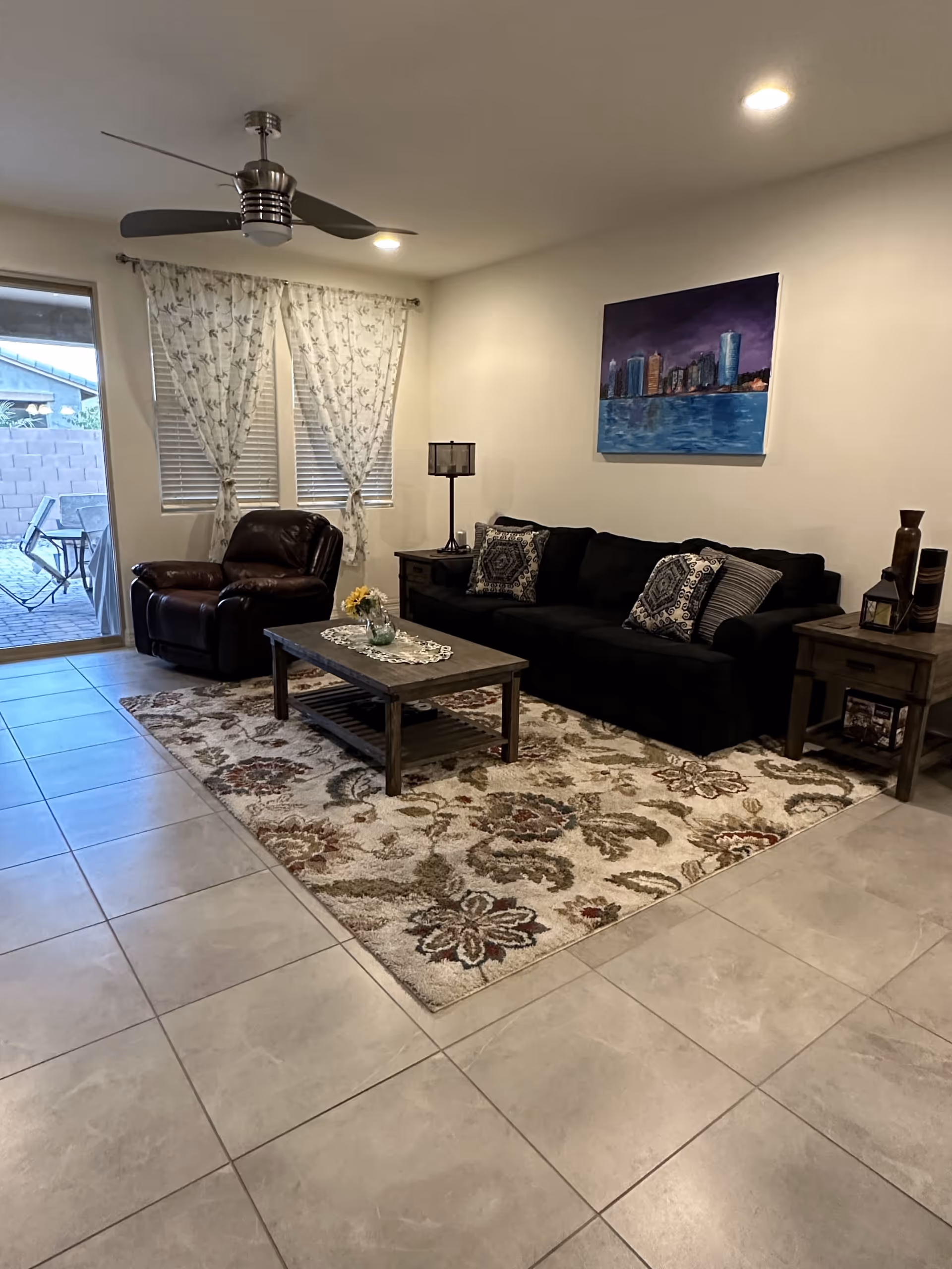 A comfortable living room with a dark sofa, recliner, coffee table, rug, and patio door.