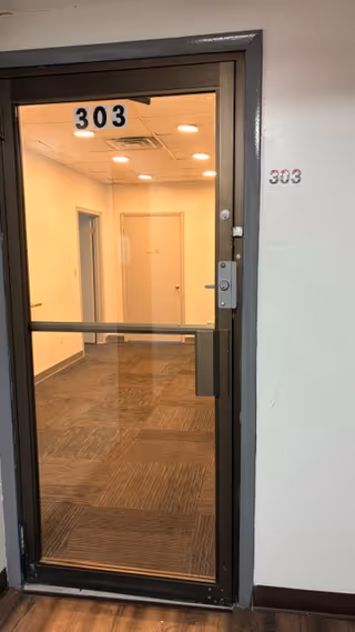 Interior hallway through a glass door labeled 303, with overhead ceiling lights.