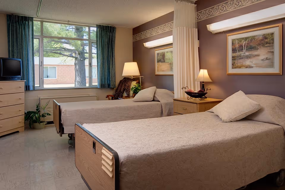 Bright senior living bedroom with two twin beds, dressers, lamps, and a window.